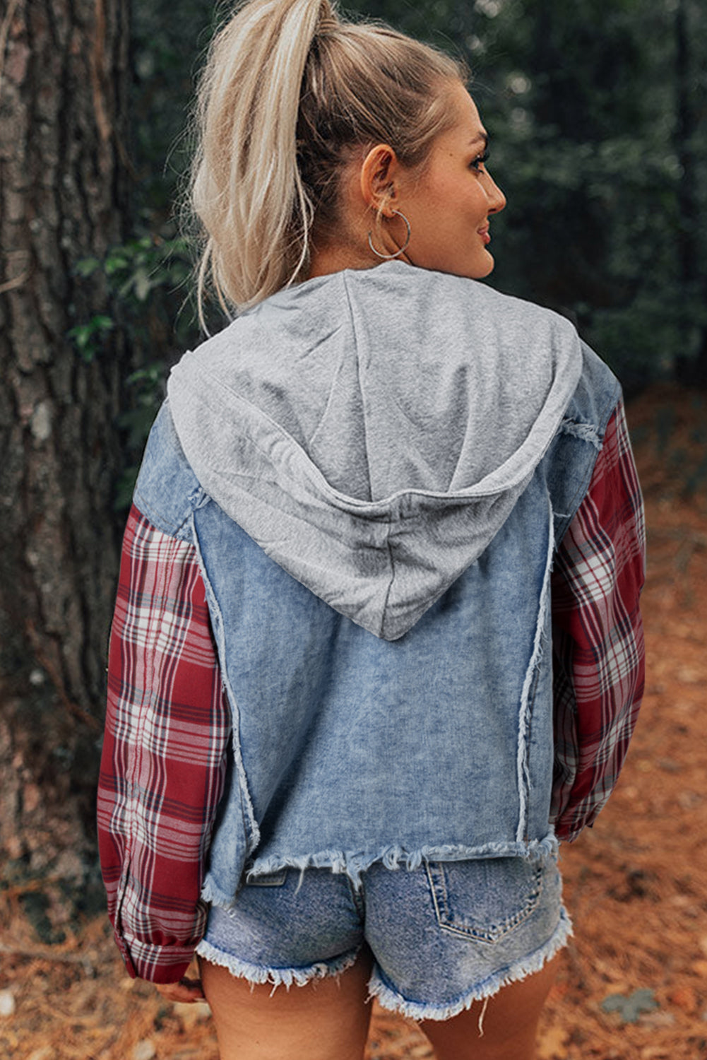 Blond woman wearing denim jacket with red and white plaid sleeves, flap pockets, hood, and button up closure. back view