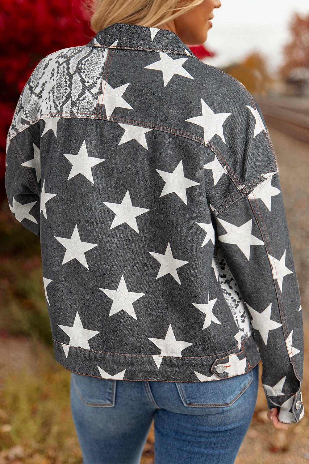 blond woman wearing black denim jacket printed with snakeskin and stars. back close up view