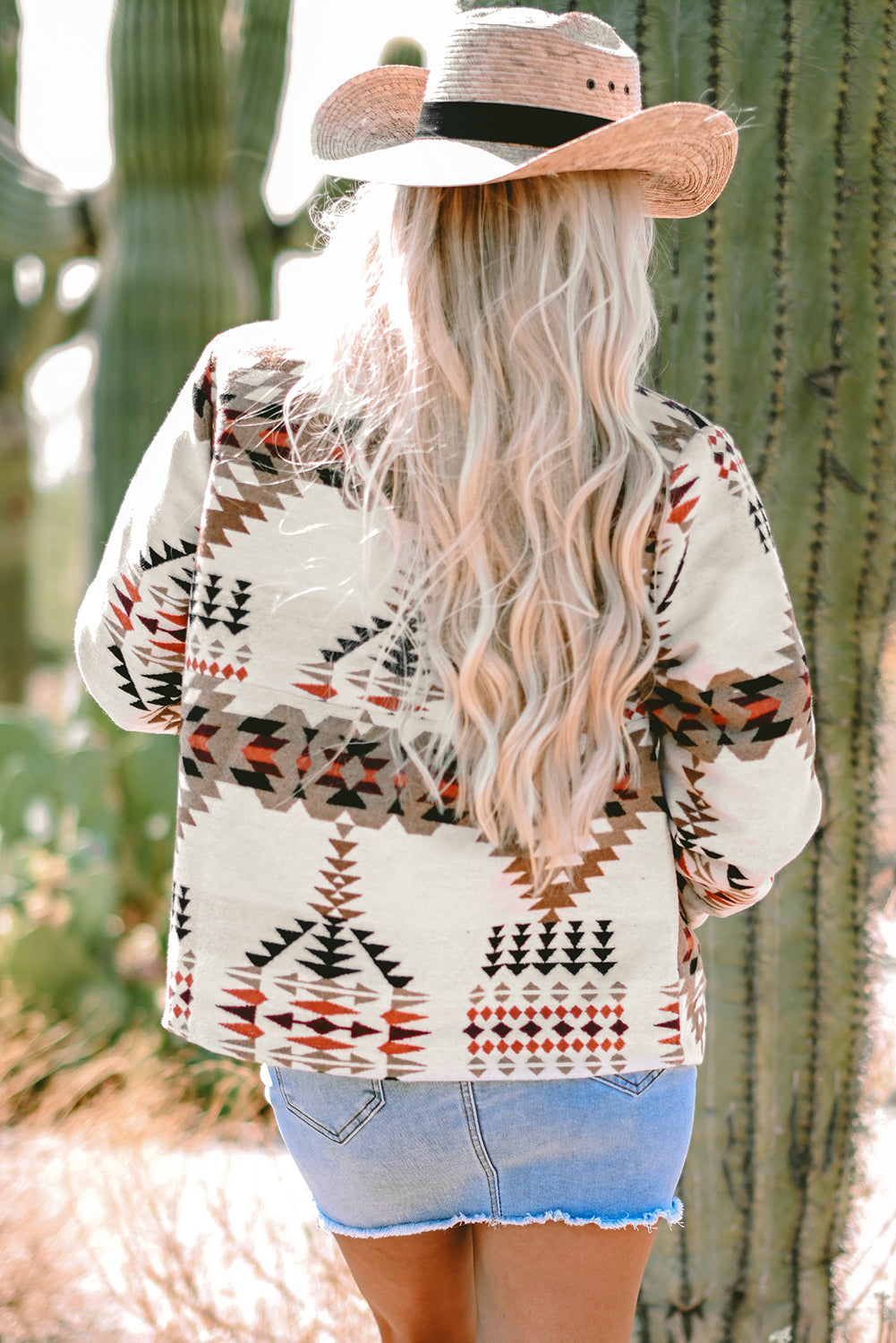 Cowgirl wearing featured Aztec Printed Zip Up Jacket in Beige, paired with a denim mini skirt, and tan cowboy hat. Back view