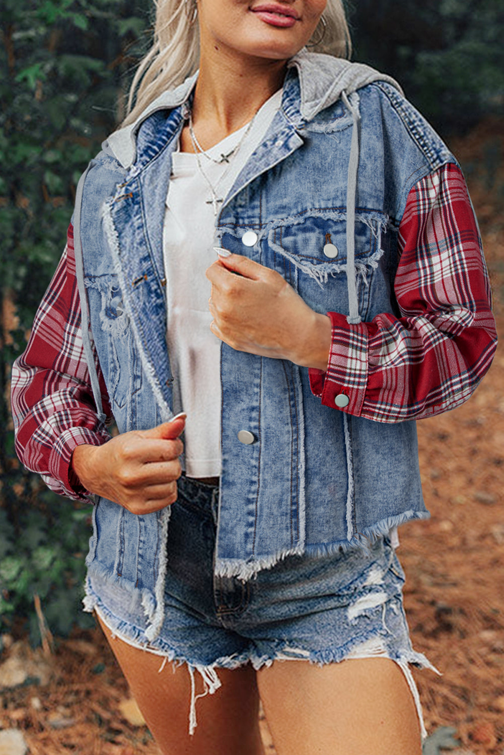 Blond woman wearing denim jacket with red and white plaid sleeves, flap pockets, hood, and button up closure. Front open view