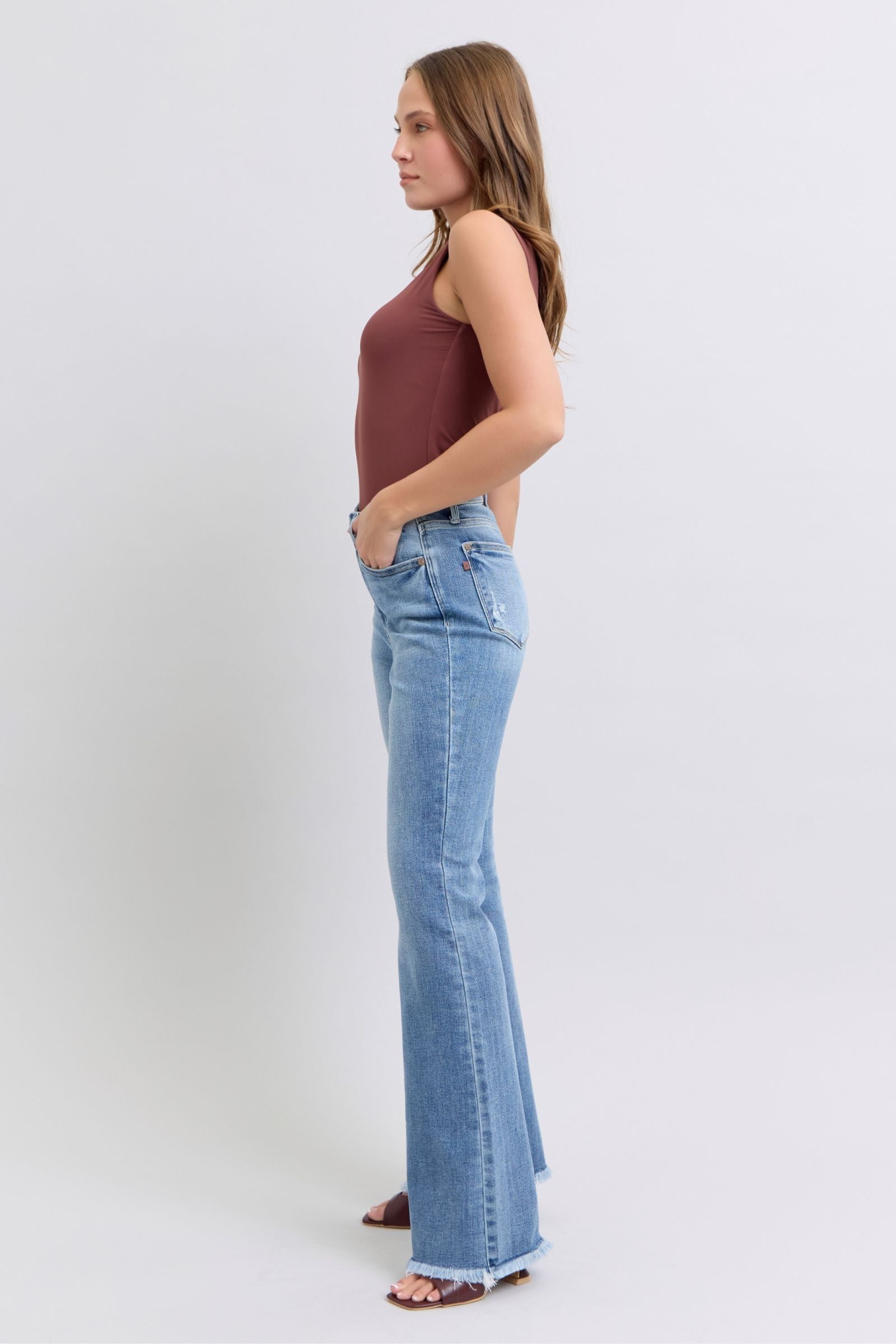 Judy Blue Raw hem high rise bootcut jeans are a trendy and stylish denim option for a fashionable look. These jeans feature a high-rise waist that sits above the natural waistline, elongating the legs and providing a flattering silhouette. The bootcut style flares out slightly from the knee down, creating a balanced and vintage-inspired look. The raw hem detail at the bottom adds a modern and edgy touch to the jeans, giving them a unique and on-trend appearance.  Left side view