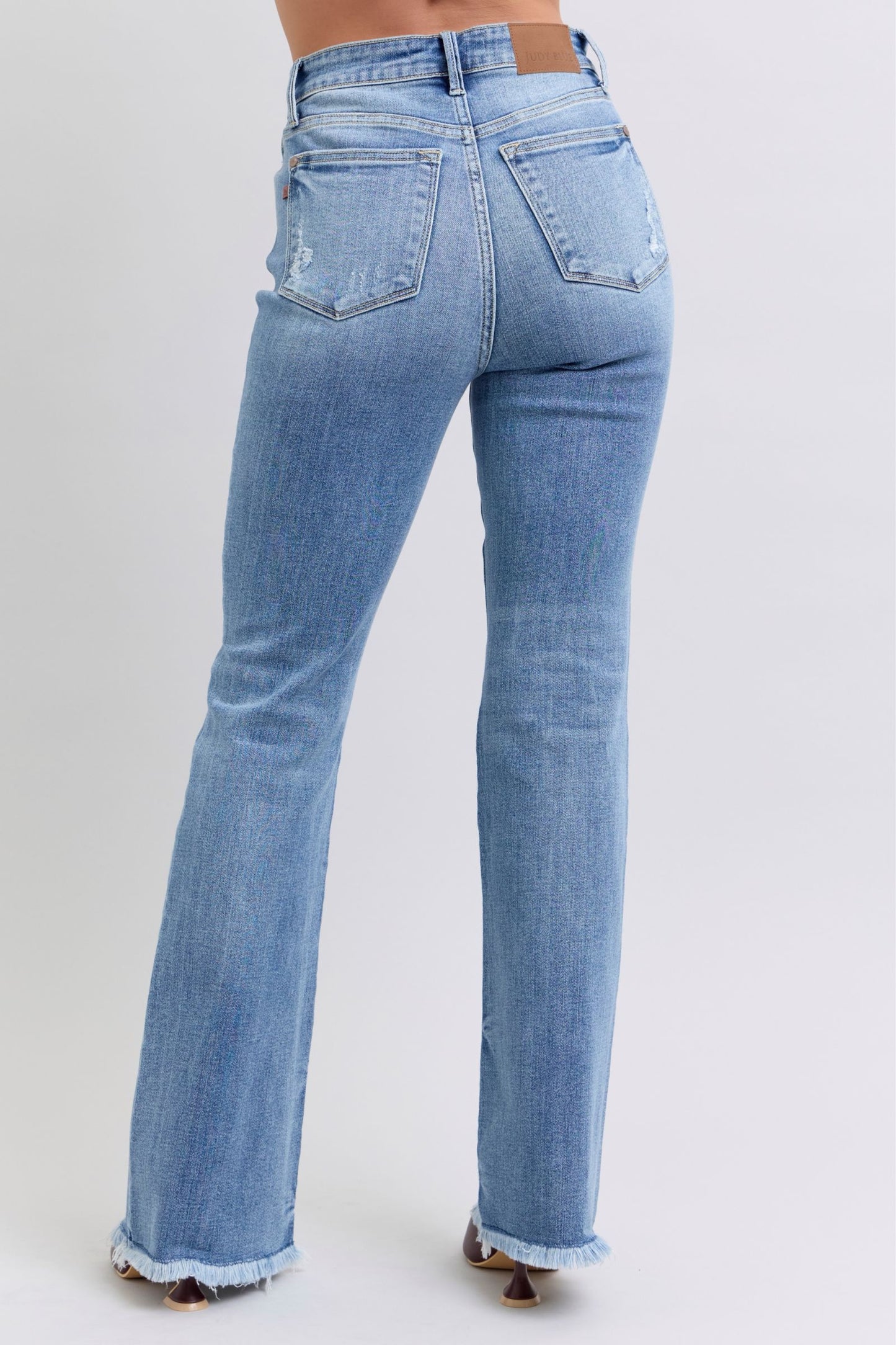 Judy Blue Raw hem high rise bootcut jeans are a trendy and stylish denim option for a fashionable look. These jeans feature a high-rise waist that sits above the natural waistline, elongating the legs and providing a flattering silhouette. The bootcut style flares out slightly from the knee down, creating a balanced and vintage-inspired look. The raw hem detail at the bottom adds a modern and edgy touch to the jeans, giving them a unique and on-trend appearance.  Back view
