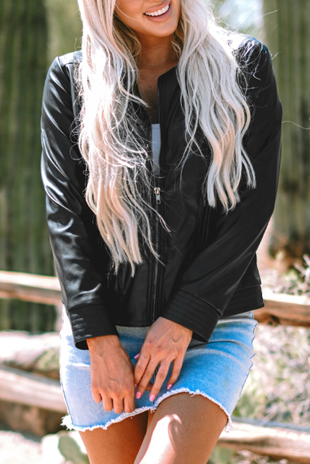Young blond woman wearing faux leather black bomber jacket & denim skirt, front view close up