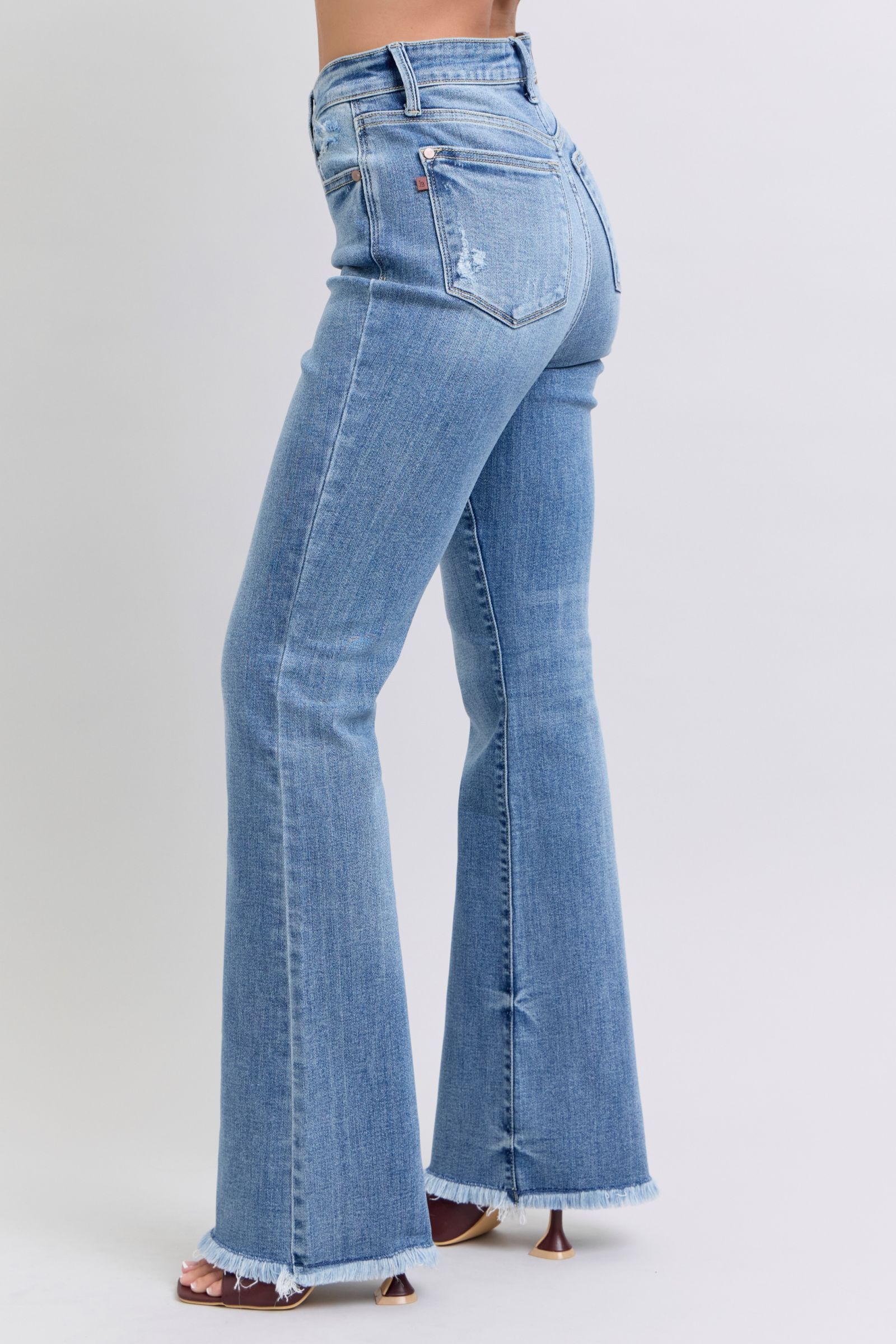 Judy Blue Raw hem high rise bootcut jeans are a trendy and stylish denim option for a fashionable look. These jeans feature a high-rise waist that sits above the natural waistline, elongating the legs and providing a flattering silhouette. The bootcut style flares out slightly from the knee down, creating a balanced and vintage-inspired look. The raw hem detail at the bottom adds a modern and edgy touch to the jeans, giving them a unique and on-trend appearance.  Left side view