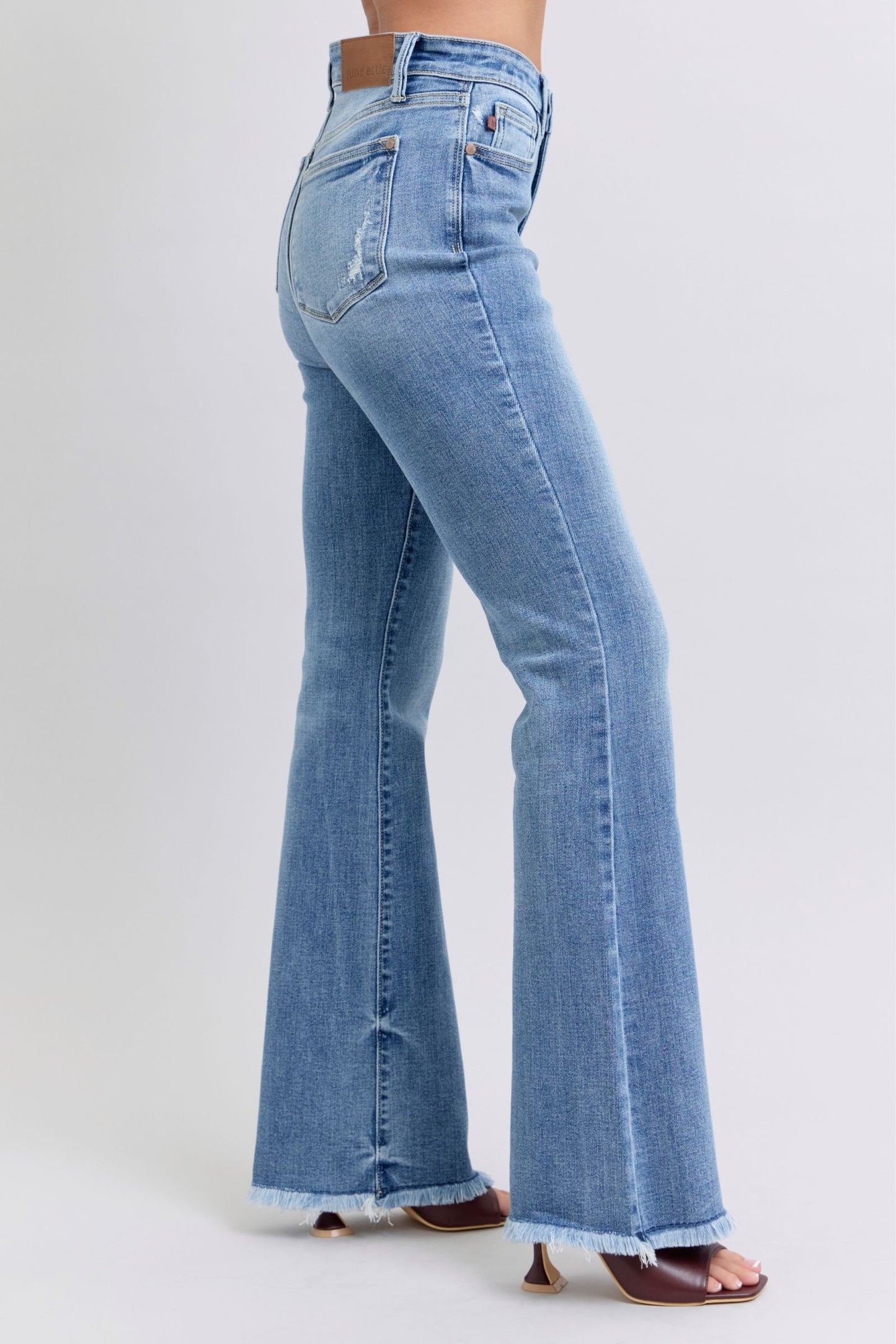Judy Blue Raw hem high rise bootcut jeans are a trendy and stylish denim option for a fashionable look. These jeans feature a high-rise waist that sits above the natural waistline, elongating the legs and providing a flattering silhouette. The bootcut style flares out slightly from the knee down, creating a balanced and vintage-inspired look. The raw hem detail at the bottom adds a modern and edgy touch to the jeans, giving them a unique and on-trend appearance. Right side view